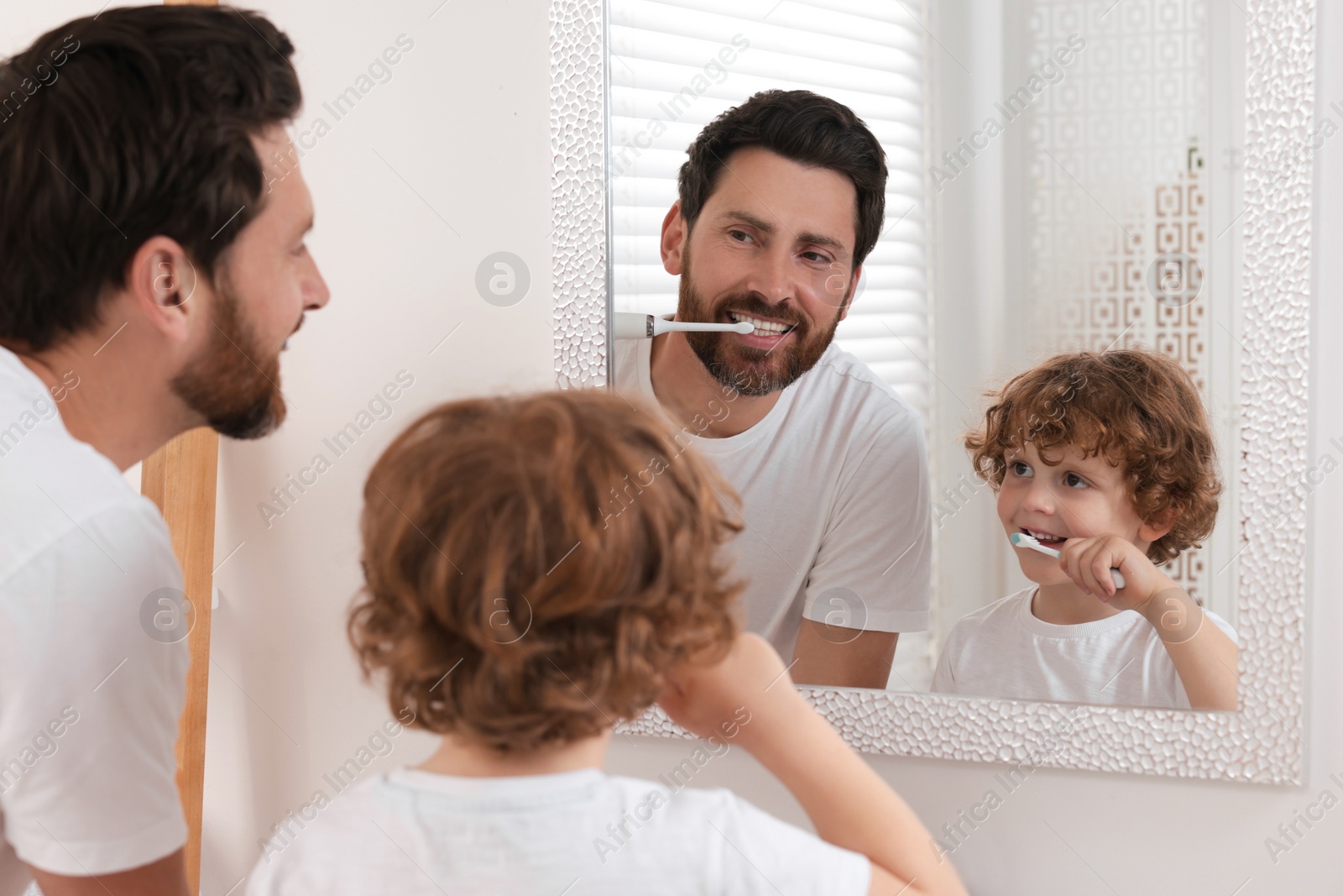 Photo of Father and his son brushing teeth together near mirror in bathroom