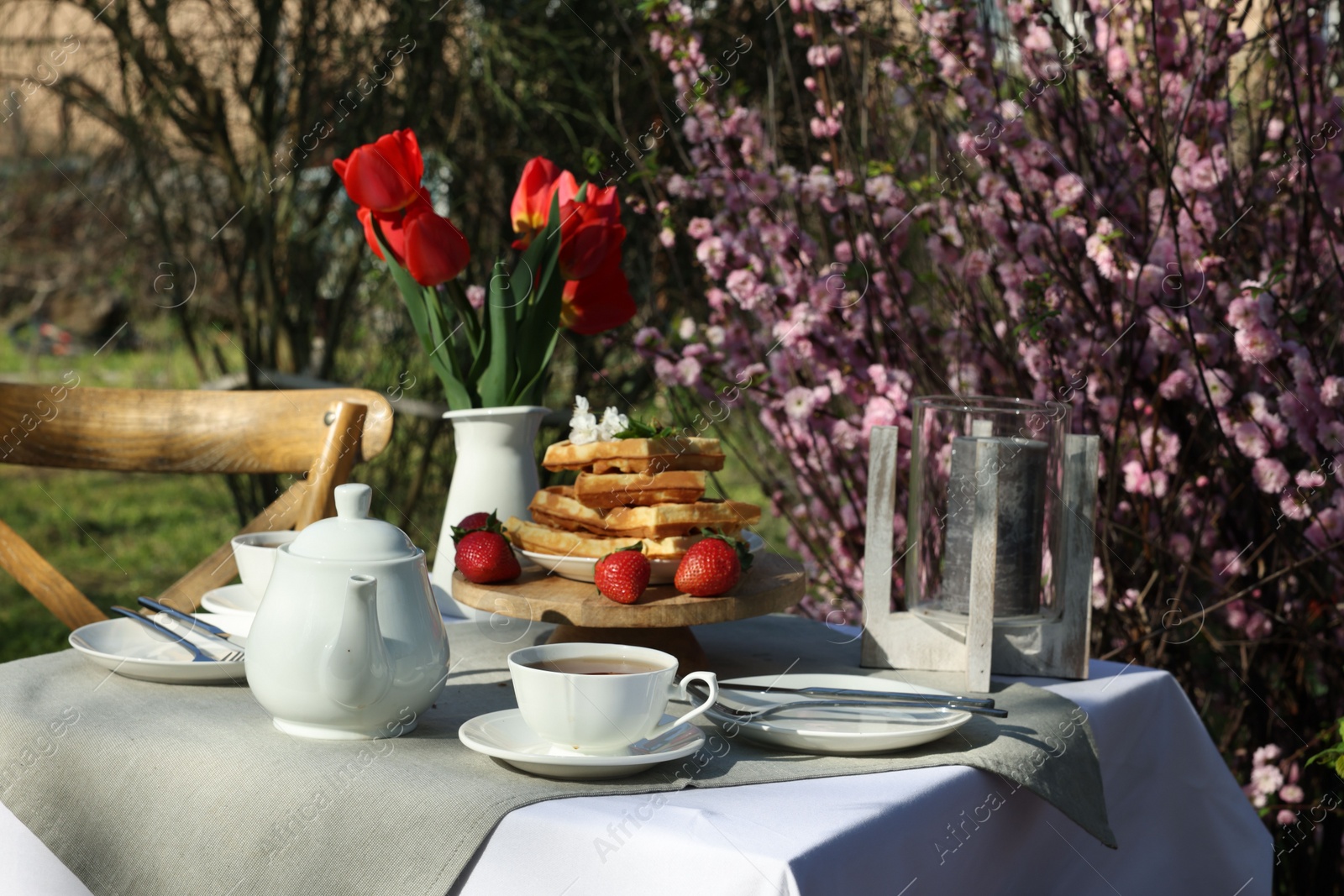 Photo of Beautiful bouquet of tulips and freshly baked waffles on table served for tea drinking in garden