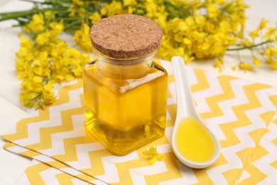 Photo of Rapeseed oil in glass bottle, gravy boat and beautiful yellow flowers on table, closeup