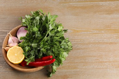 Photo of Bowl with fresh green parsley, chili peppers, lemon, onion and garlic on wooden table, above view. Space for text