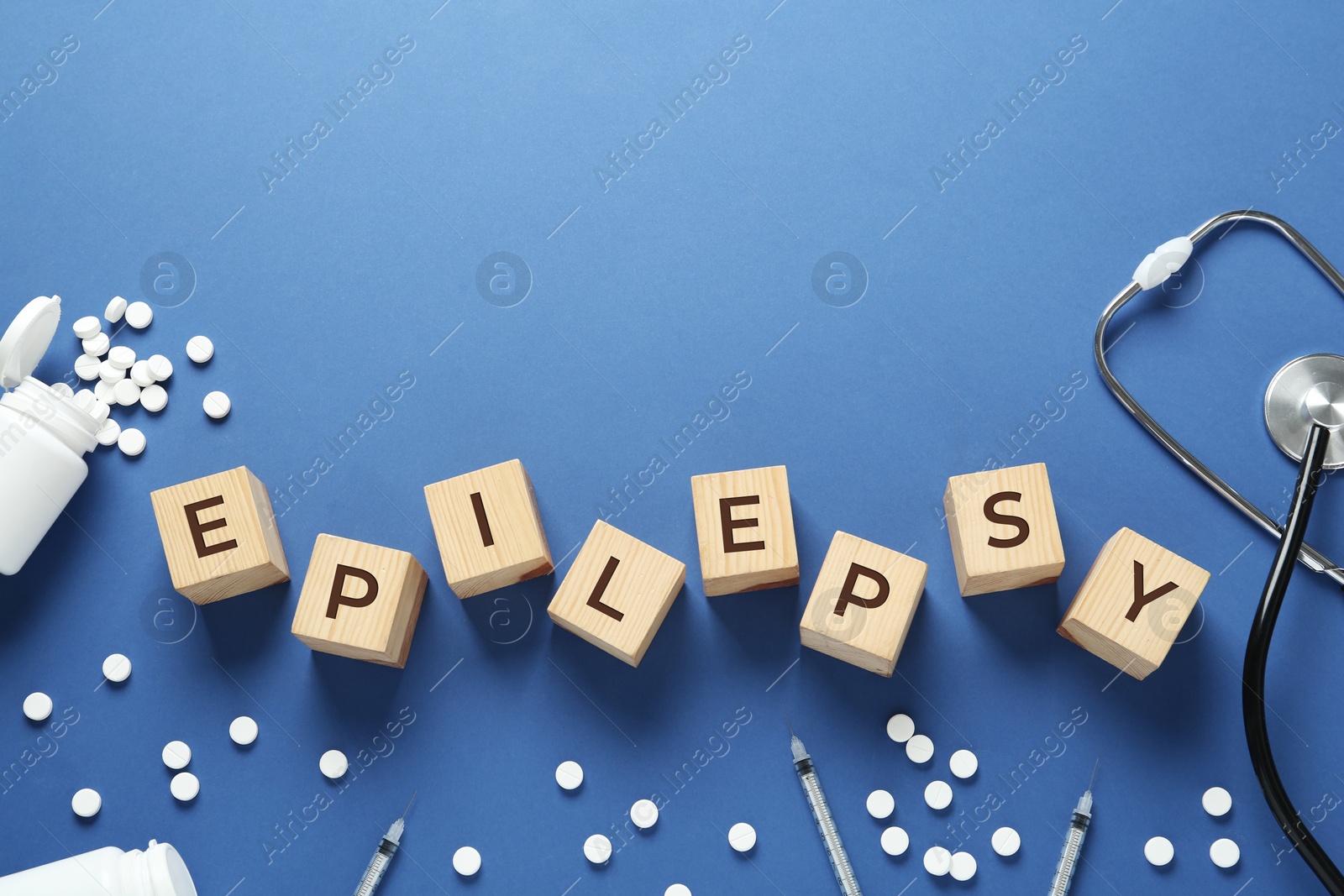 Photo of Wooden cubes with word Epilepsy, stethoscope, pills and syringes on blue background, flat lay. Space for text