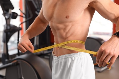 Photo of Athletic man measuring waist with tape in gym, closeup