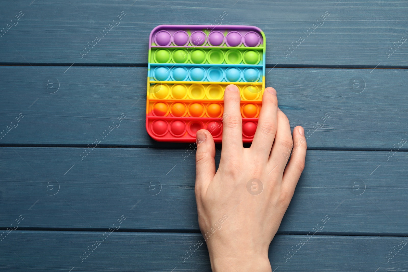 Photo of Woman using pop it fidget toy at blue wooden table, top view