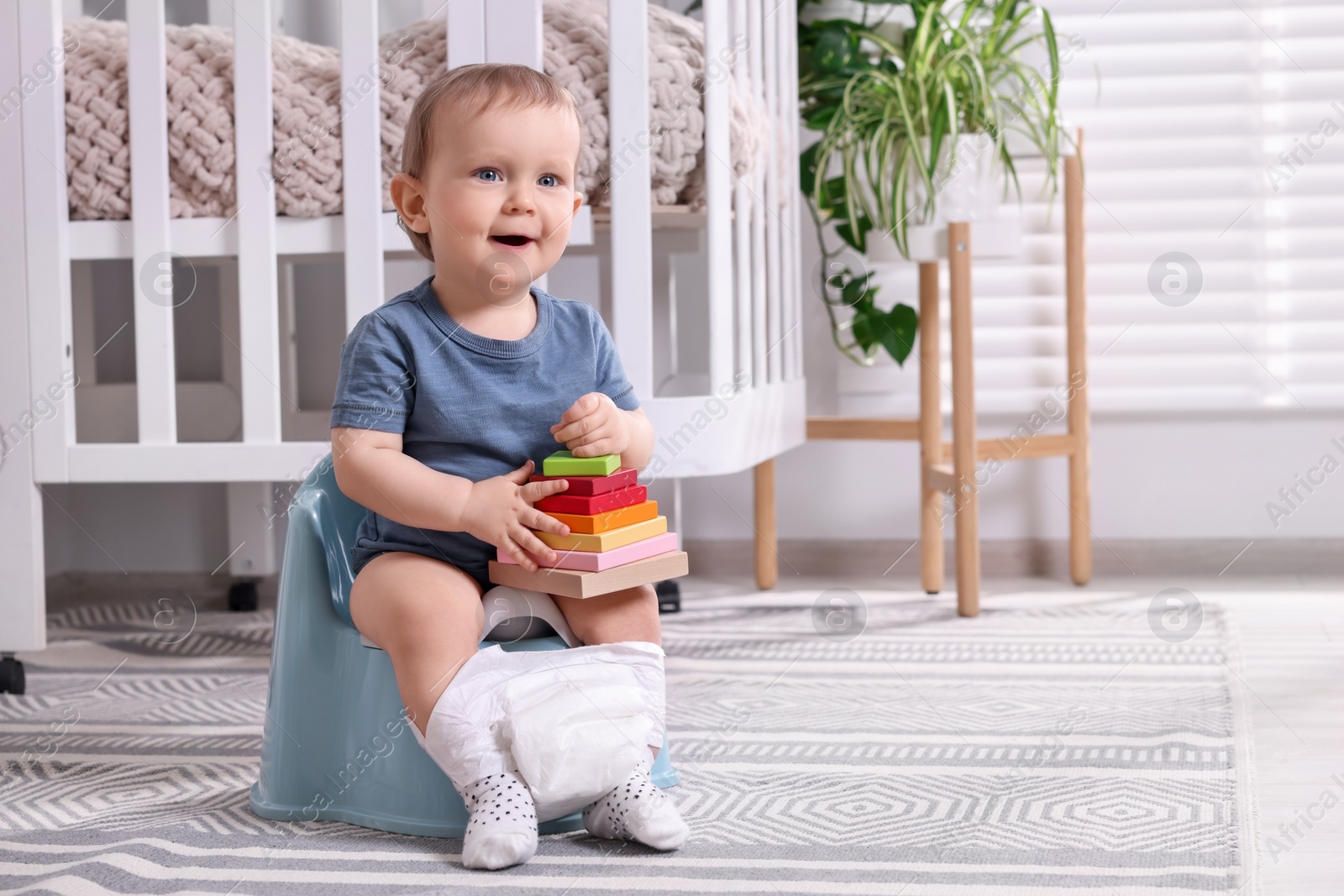 Photo of Little child with toy sitting on plastic baby potty indoors. Space for text