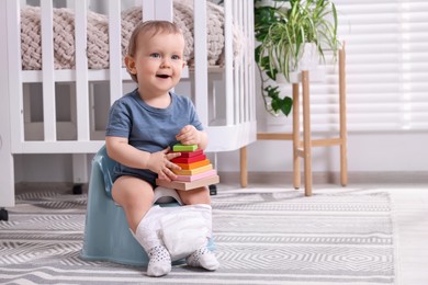 Photo of Little child with toy sitting on plastic baby potty indoors. Space for text