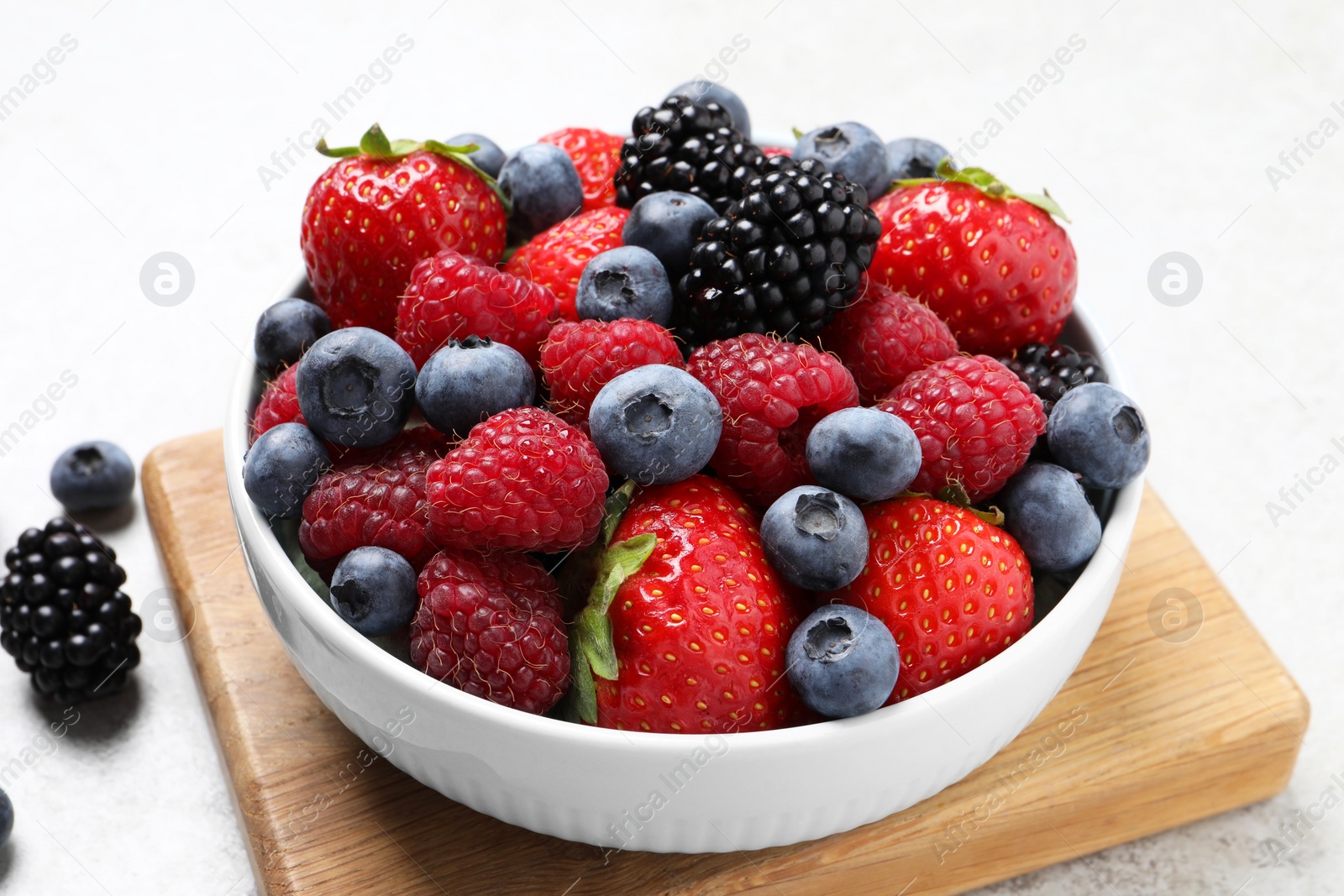 Photo of Many different fresh ripe berries in bowl on light grey table, closeup