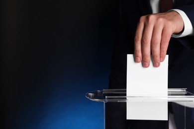 Photo of Man putting his vote into ballot box on dark blue background, closeup. Space for text