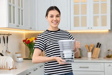 Woman holding filter jug with water in kitchen