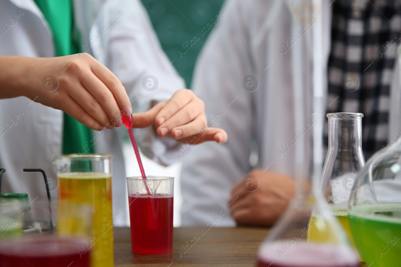 Photo of Teacher with pupil making experiment at table in chemistry class, focus on hand