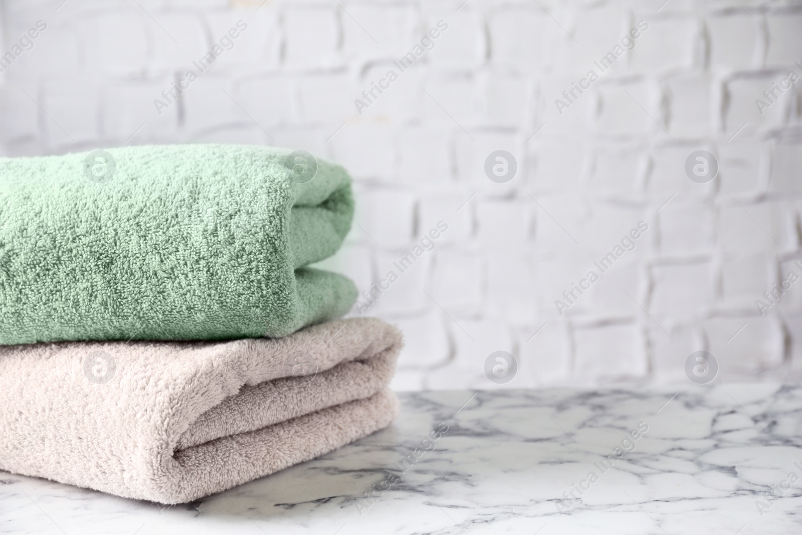 Photo of Stack of clean bath towels on white marble table. Space for text