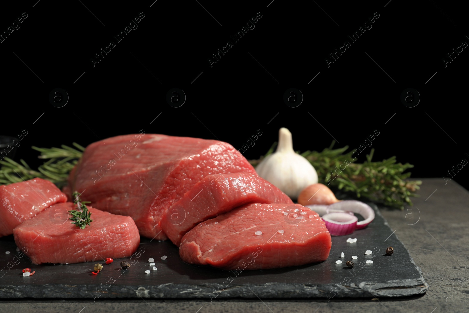 Photo of Slate plate with fresh raw meat on table against dark background