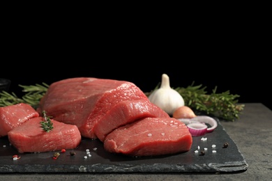 Photo of Slate plate with fresh raw meat on table against dark background