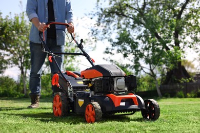 Photo of Man cutting green grass with lawn mower in garden, selective focus