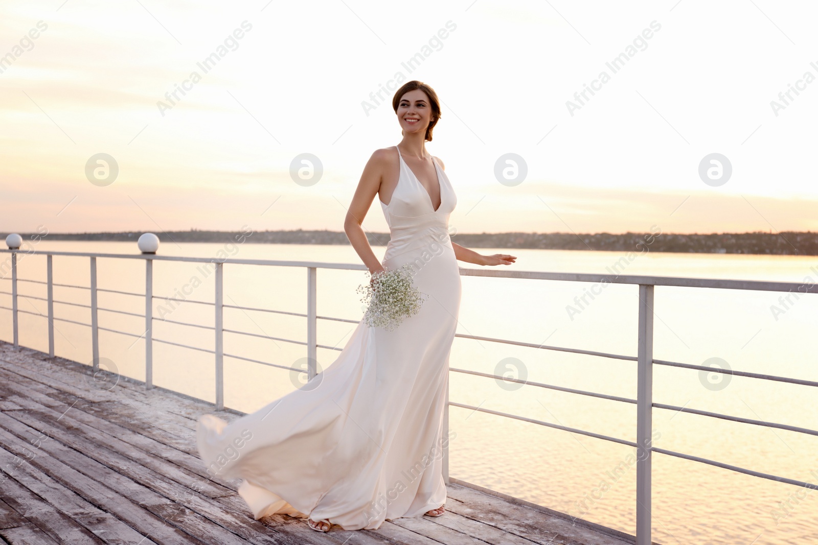 Photo of Gorgeous bride in beautiful wedding dress with bouquet near river on sunset