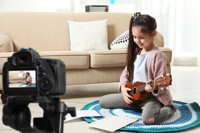 Image of Little music teacher recording guitar lesson indoors