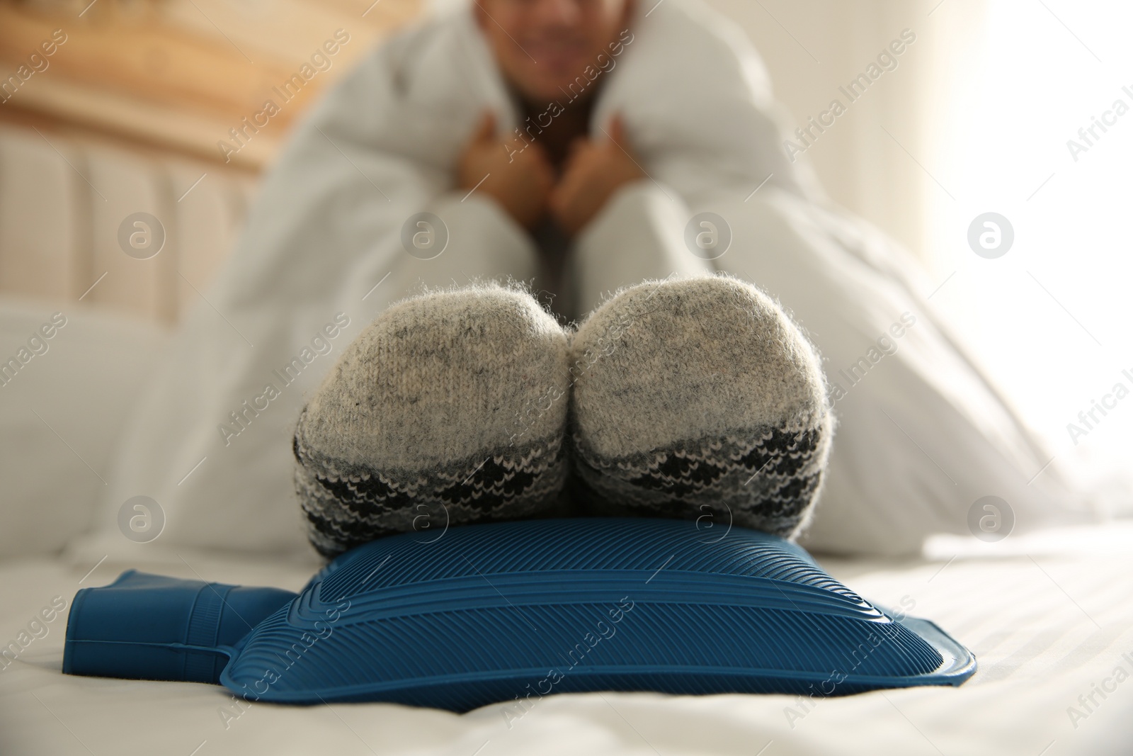 Photo of Man warming feet with hot water bottle on bed, closeup