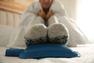 Man warming feet with hot water bottle on bed, closeup