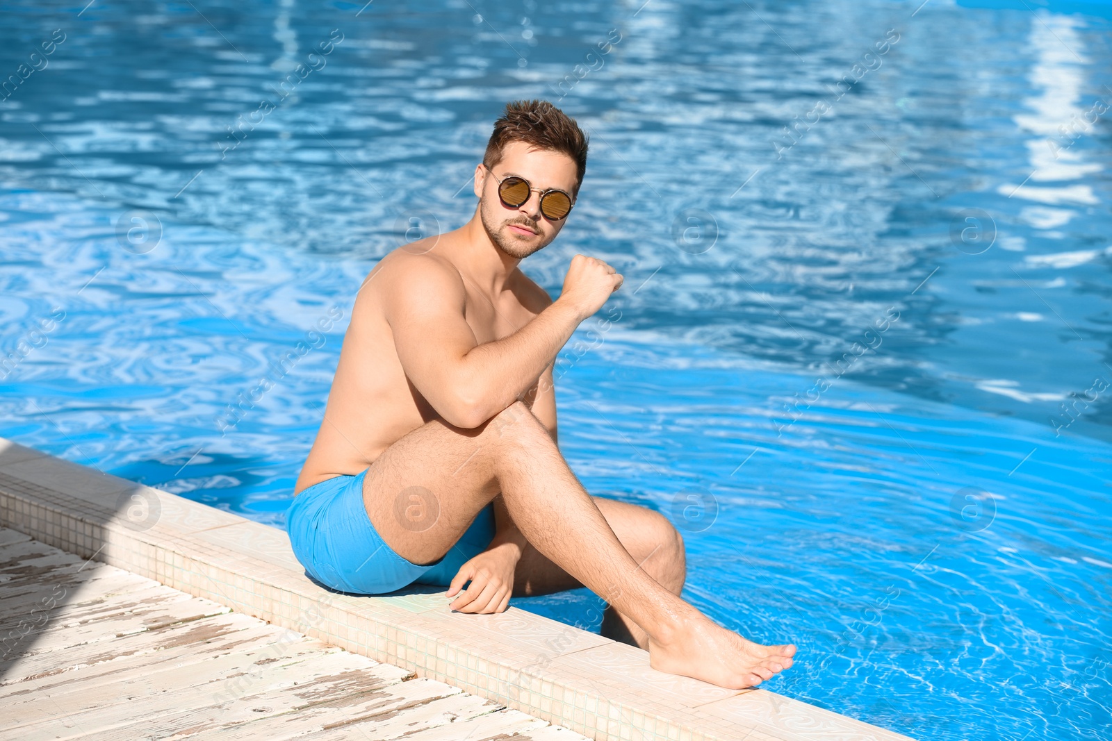 Photo of Handsome young man sitting at swimming pool edge on sunny day