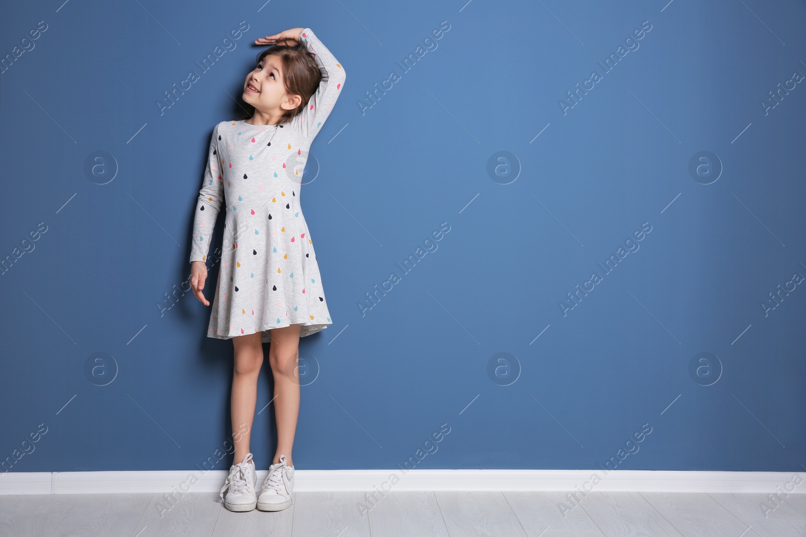 Photo of Little girl measuring her height near color wall