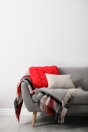 Sofa with soft pillows and warm plaids near light wall indoors. Space for text