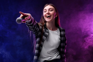 Image of Emotional woman with microphone singing on stage in color lighted smoke