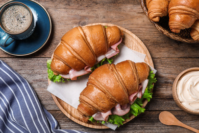 Photo of Tasty croissant sandwiches with ham on wooden table, flat lay