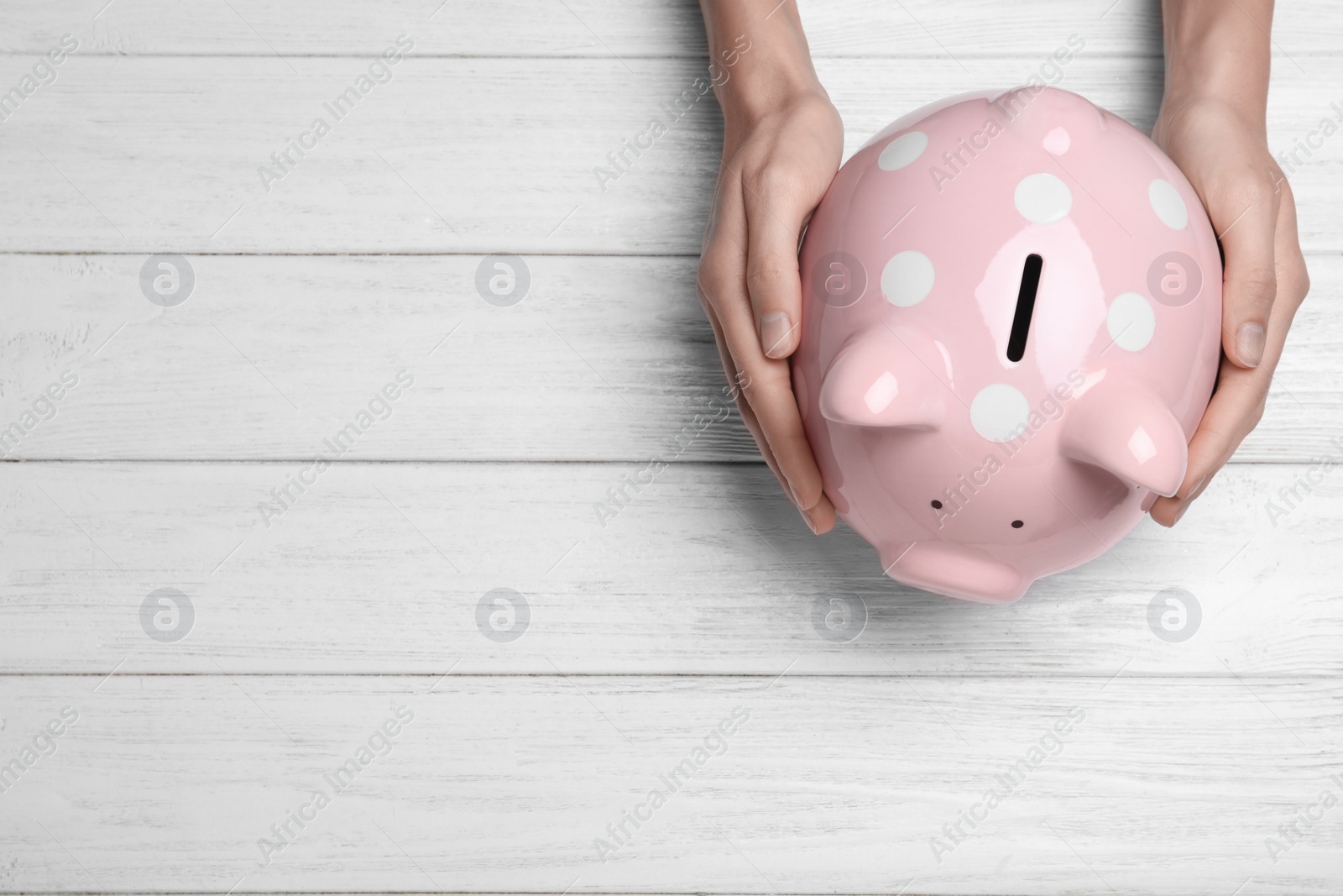 Photo of Woman holding piggy bank on white wooden table, top view with space for text. Money savings