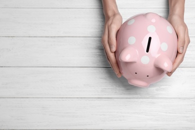 Photo of Woman holding piggy bank on white wooden table, top view with space for text. Money savings
