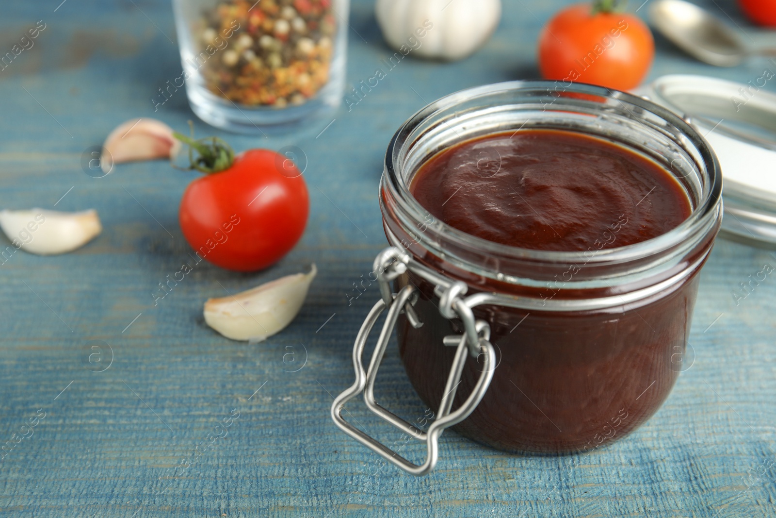 Photo of Jar with tasty barbecue sauce on blue wooden table. Space for text