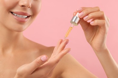 Photo of Young woman applying serum onto her hand on pink background, closeup