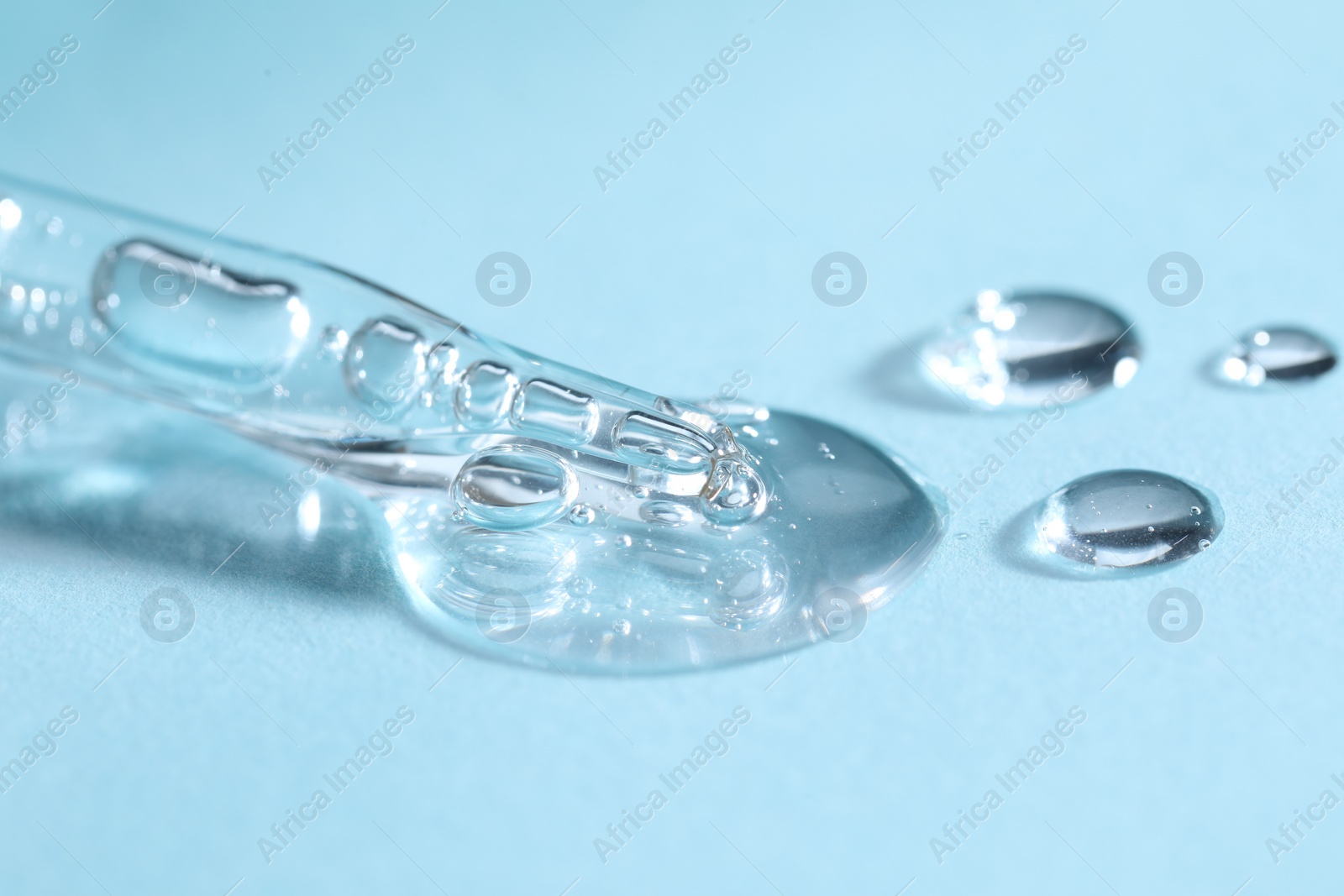 Photo of Glass pipette and transparent liquid on light blue background, closeup