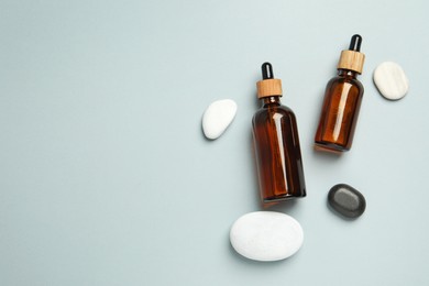 Photo of Flat lay composition with bottles of face serum and spa stones on light grey background. Space for text