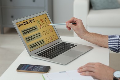 Man taking online test on laptop at desk indoors, closeup