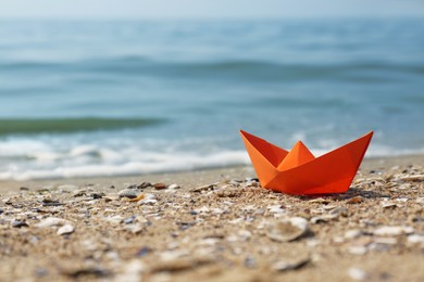 Orange paper boat on sandy beach near sea, space for text