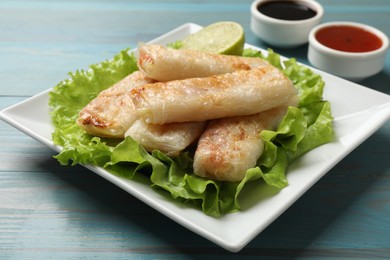 Photo of Delicious fried spring rolls served on light blue wooden table, closeup