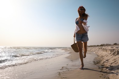 Woman with beach bag walking on sunlit seashore