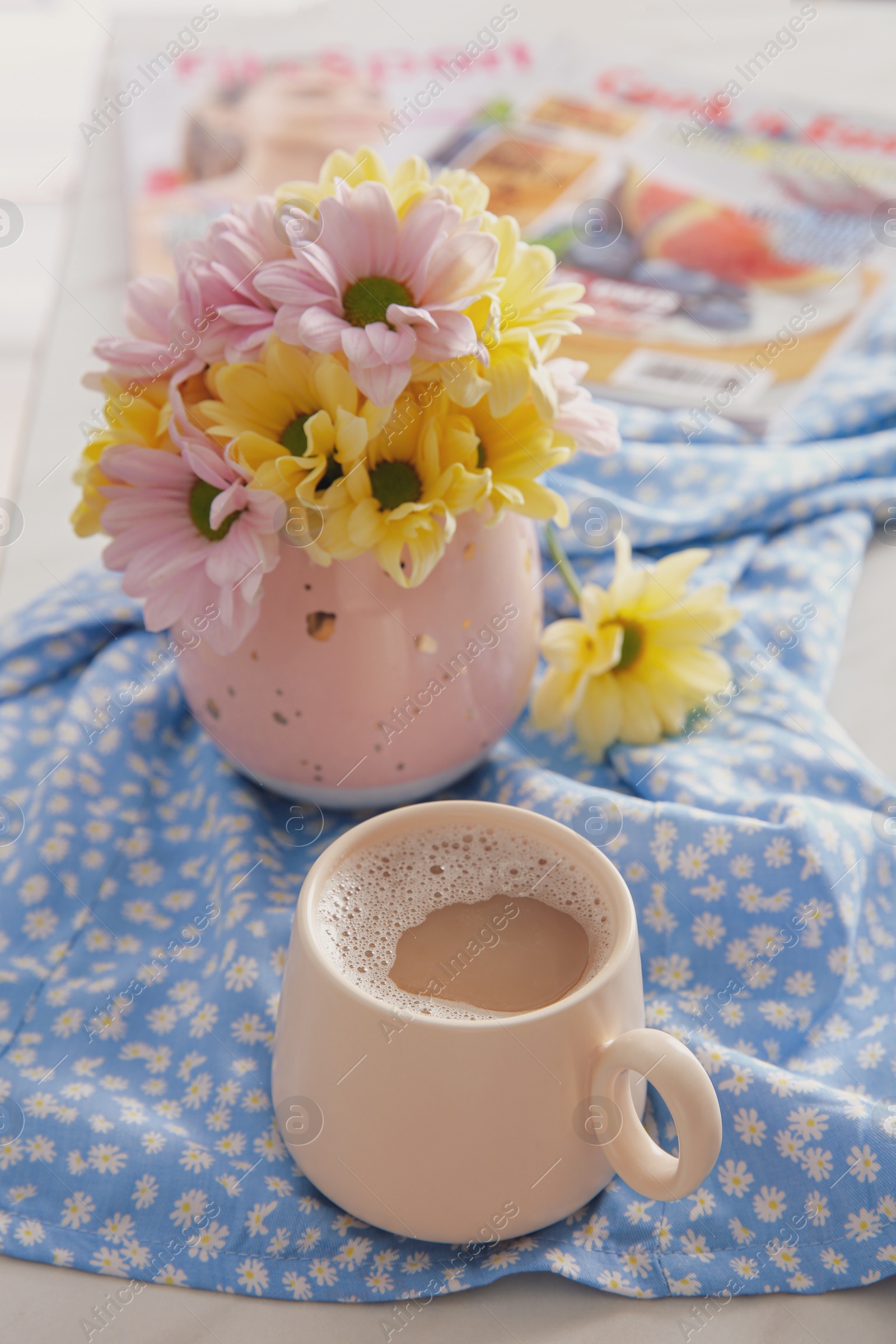 Photo of Cup of fresh coffee and beautiful bouquet on light blue printed cloth. Good morning