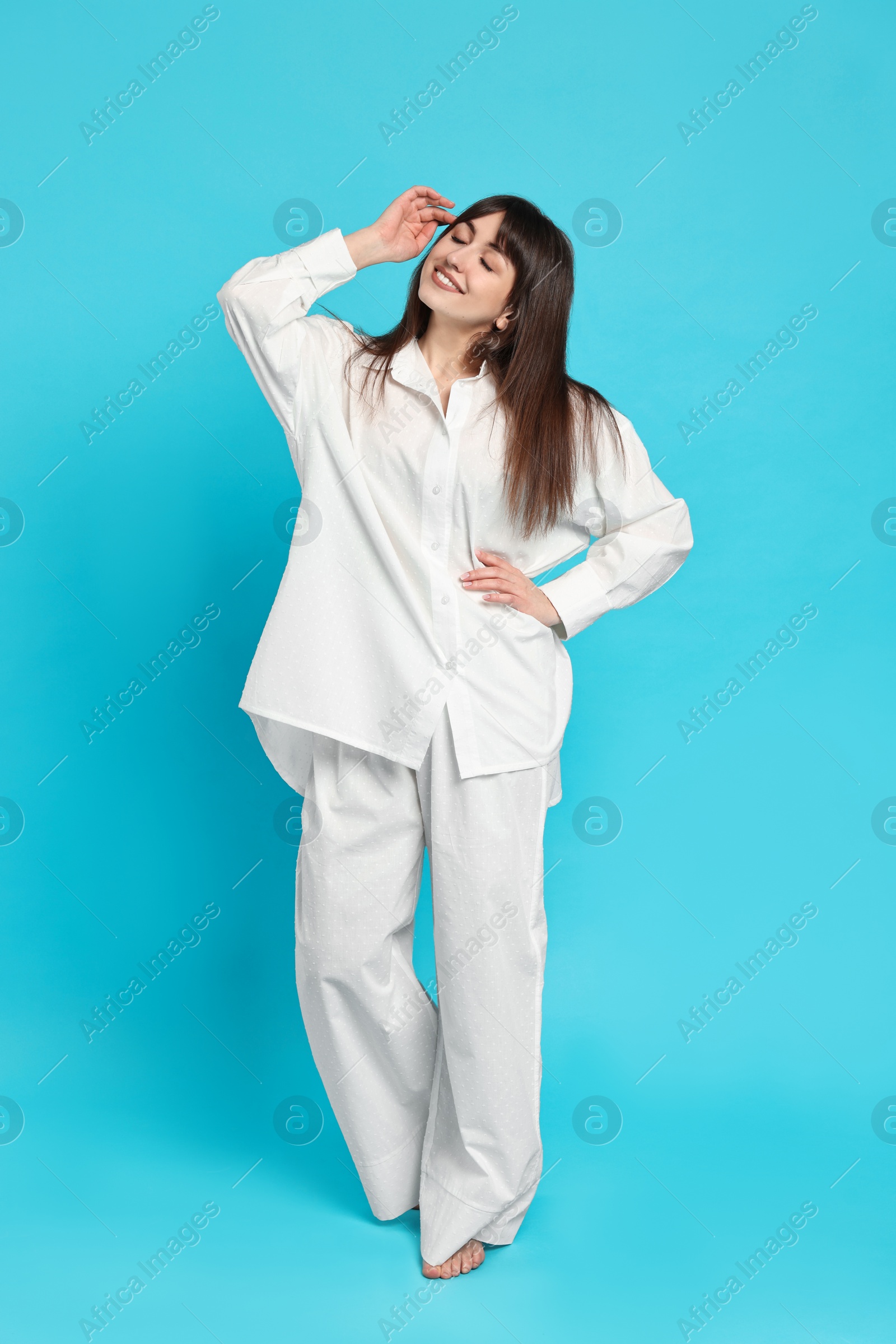 Photo of Happy woman wearing pyjama on light blue background