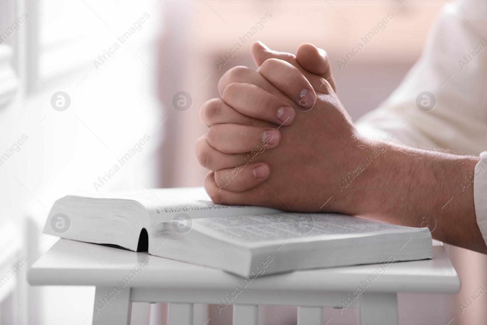 Photo of Religion. Christian man praying over Bible indoors, closeup