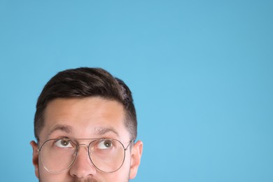 Photo of Man in stylish glasses on light blue background, closeup. Space for text