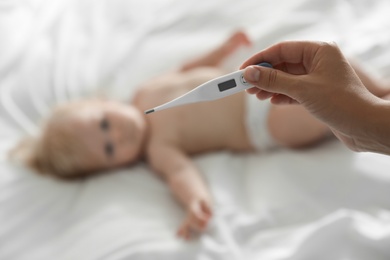 Pediatrician holding thermometer and blurred baby on background, closeup. Health care