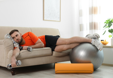 Photo of Lazy young man with sport equipment on sofa at home