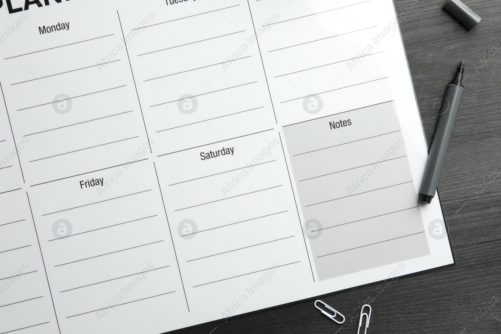 Photo of Timetable. Weekly planner, felt pen and paper clips on black wooden table, top view