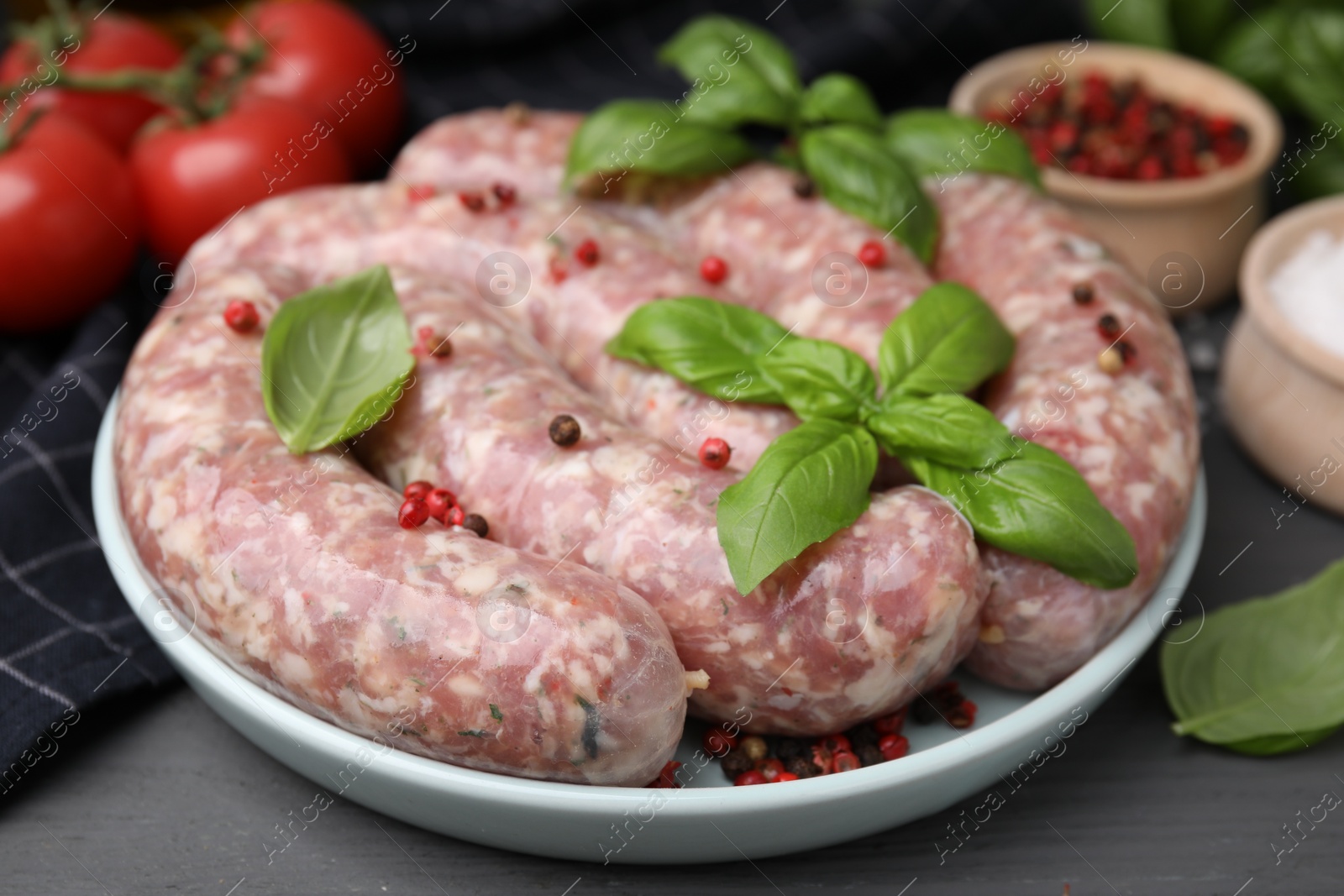 Photo of Raw homemade sausages, basil leaves and peppercorns on grey table, closeup