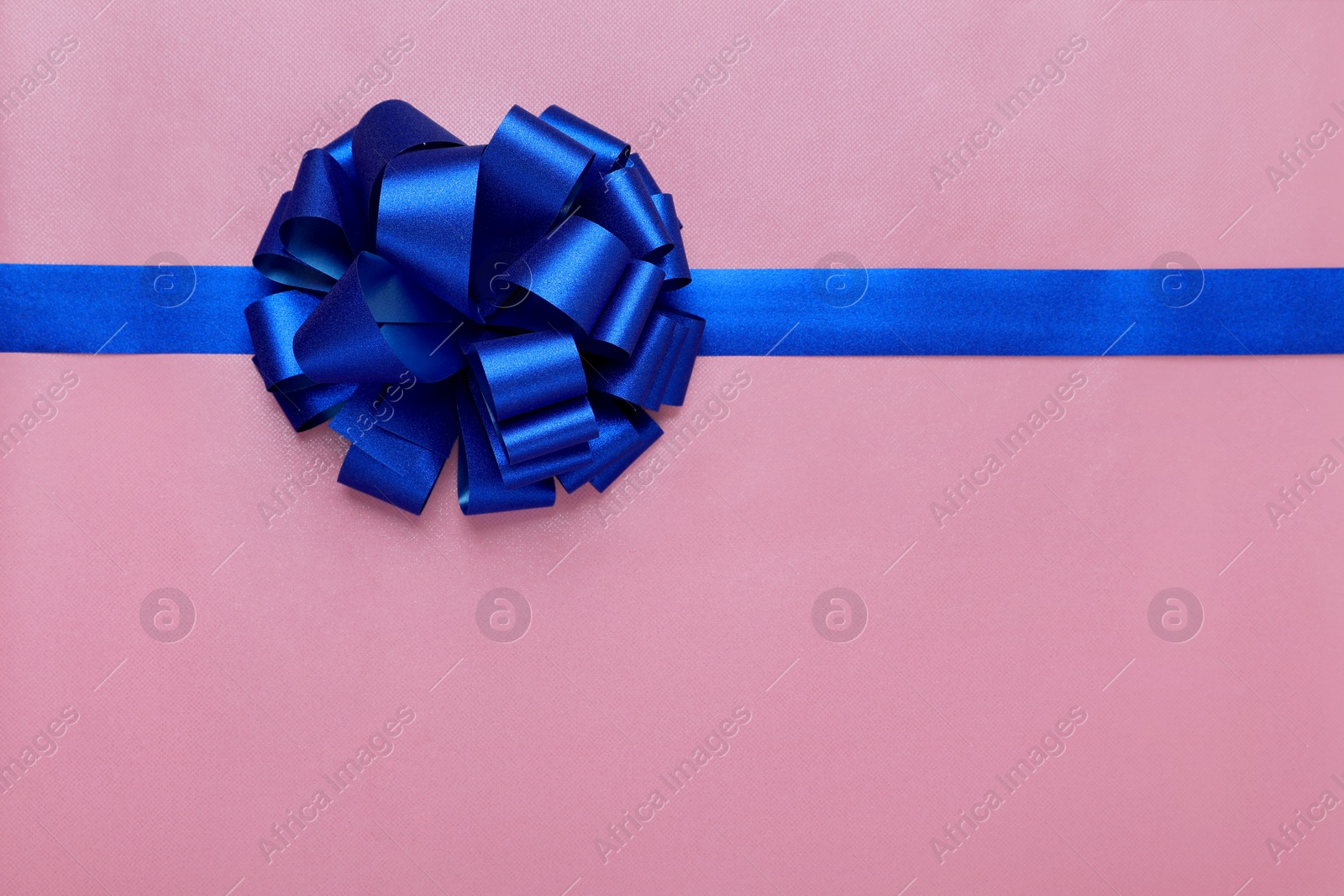 Photo of Blue ribbon with bow on pink background, top view. Space for text