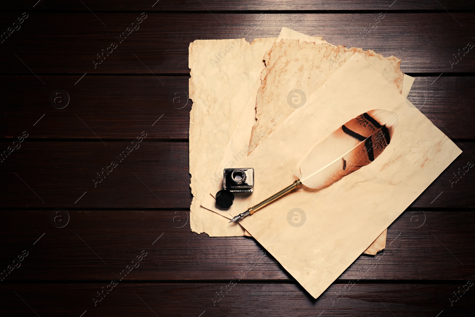 Photo of Inkwell, feather pen and vintage parchment on wooden table, flat lay. Space for text