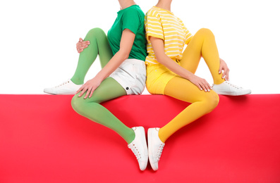 Women wearing bright tights sitting together on color background, closeup