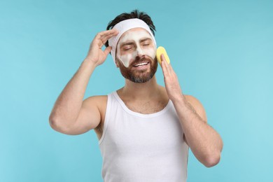 Man with headband washing his face using sponge on light blue background