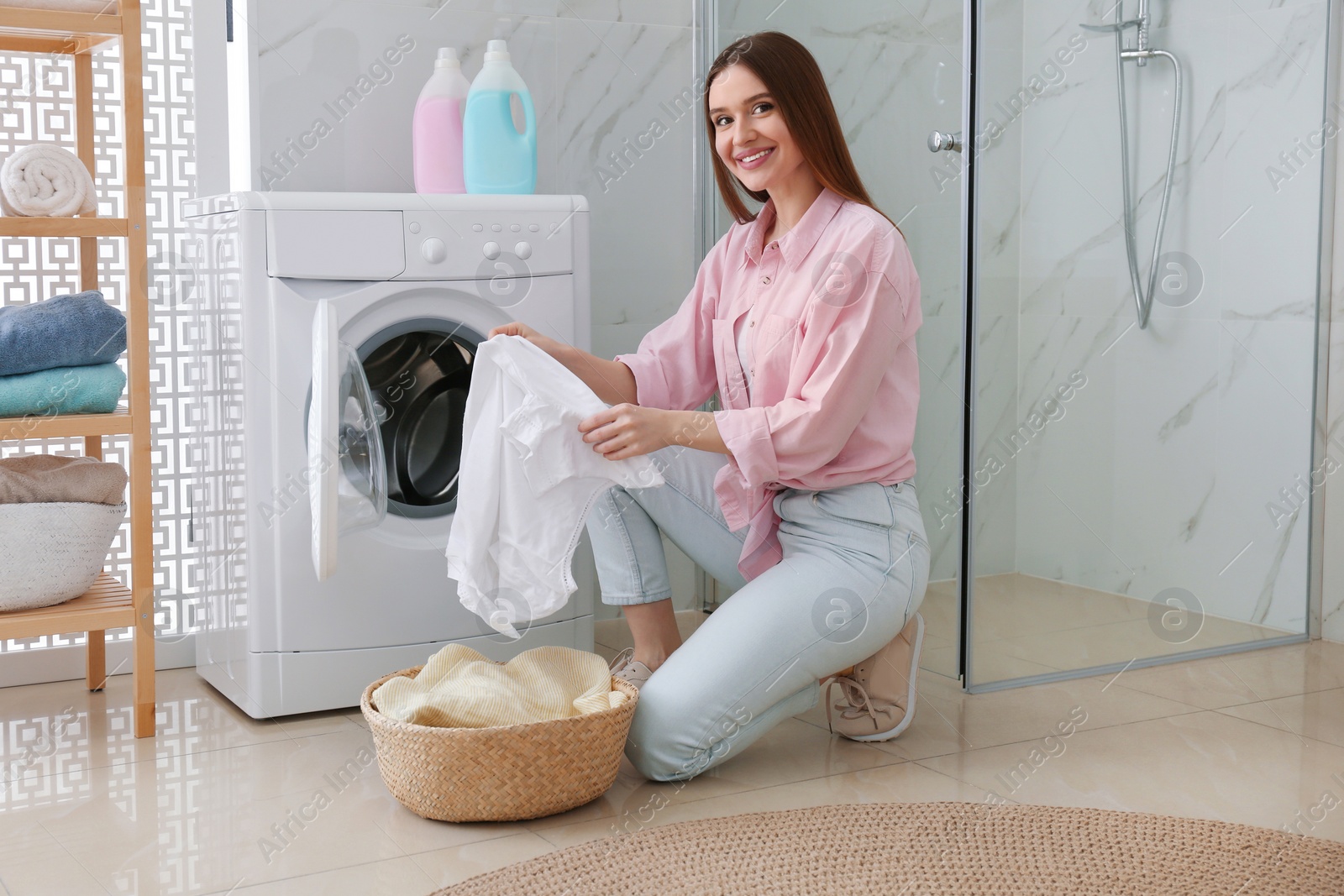 Photo of Young woman with clothes near washing machine in bathroom. Laundry day