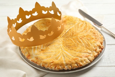 Photo of Traditional galette des Rois with paper crown on white wooden table